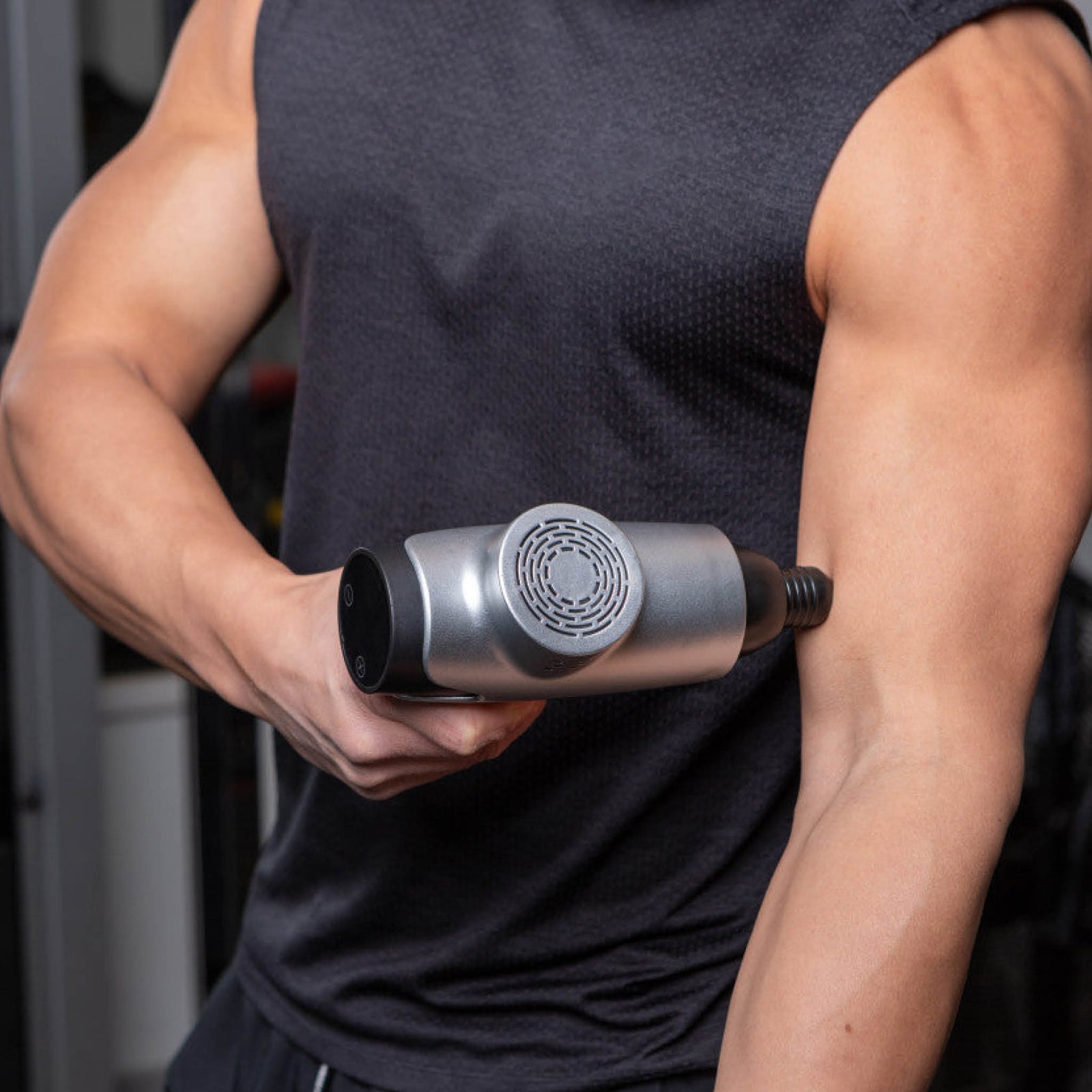 Wearing a sleeveless black shirt, a person uses the Reviber Massage Gun by Reviber on their upper arm, targeting the biceps for deep-tissue massage and supporting muscle recovery.